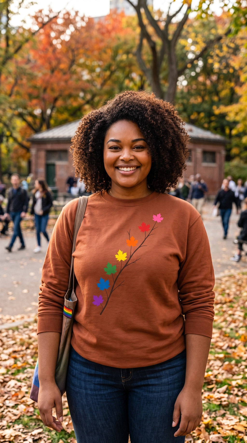 Flaunt It unisex heavyweight long sleeve shirt in brown with a pride maple leaf branch graphic, worn by a smiling woman