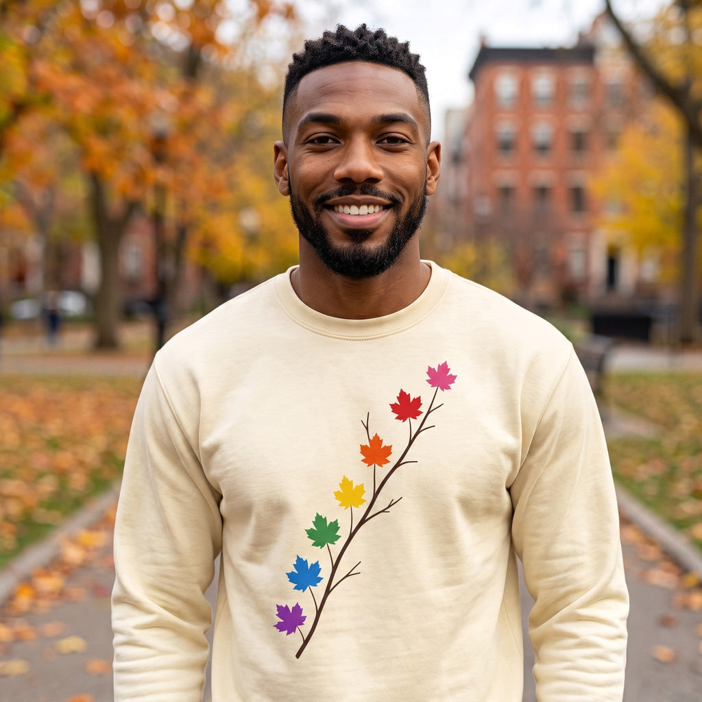 A smiling man wearing a Flaunt It cream heavyweight long sleeve shirt with a pride maple leaf branch graphic.