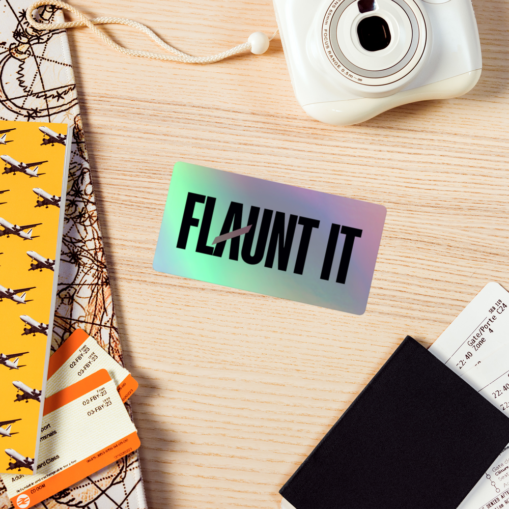 Flaunt It holographic vinyl sticker with a 3D effect on a wooden desk with travel accessories