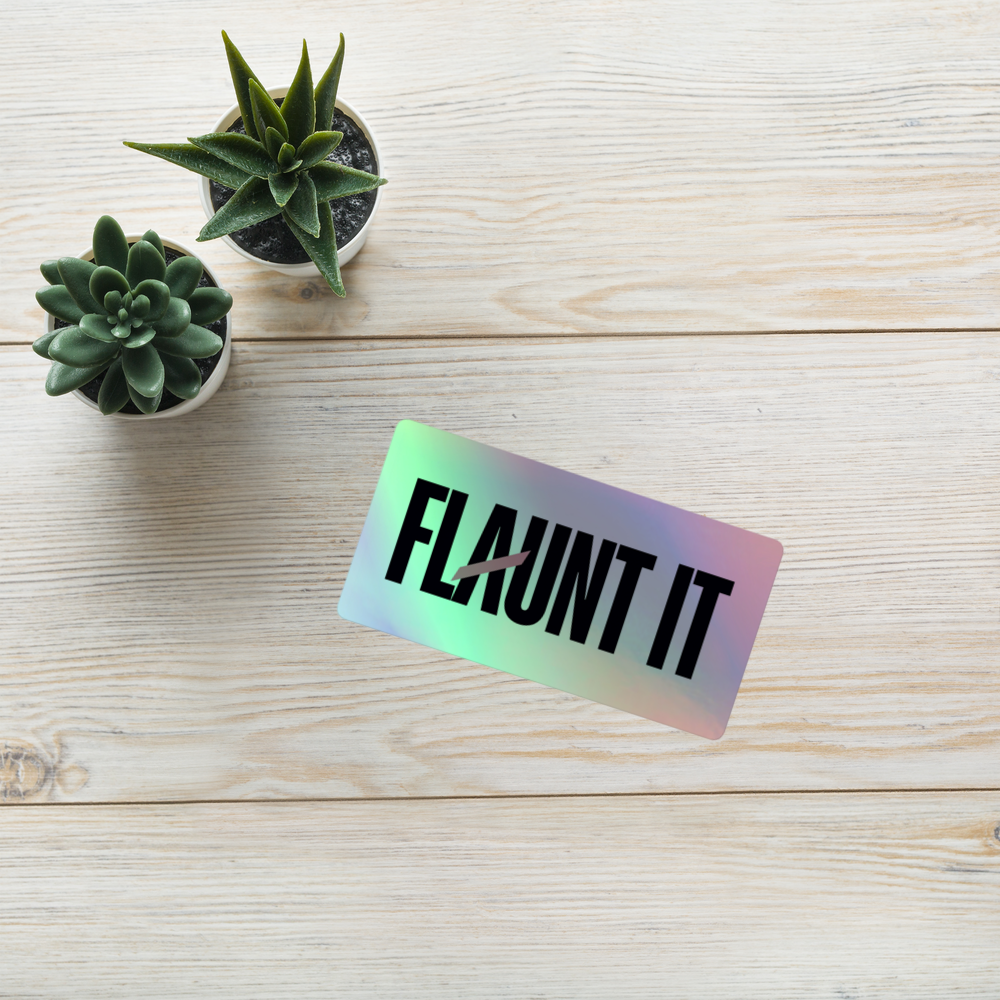 Flaunt It holographic vinyl sticker with black logo on a light wood surface next to two small potted succulents.