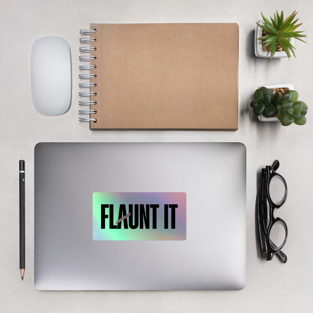 Flaunt It holographic vinyl logo sticker applied to a silver laptop on a desk with a notebook and succulents.