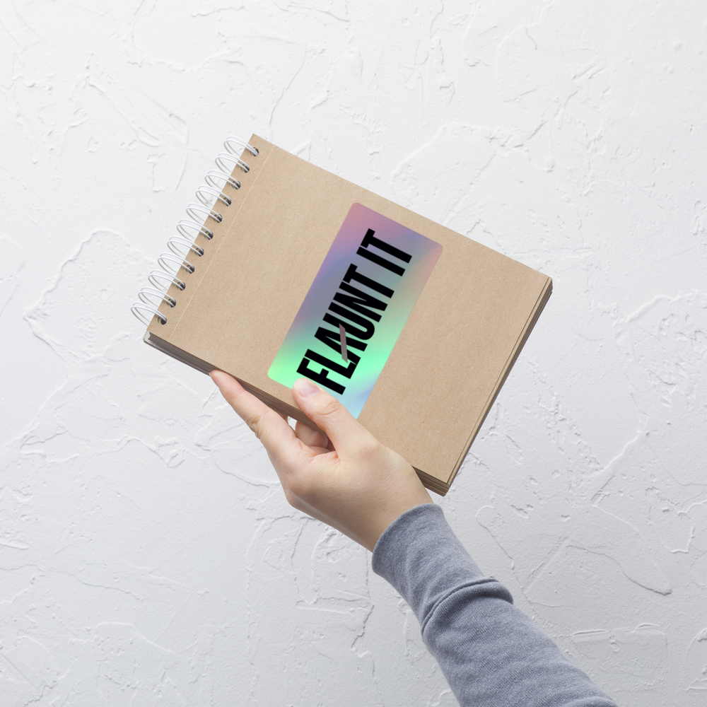 Flaunt It holographic vinyl sticker with 3D pattern on a spiral notebook held by a hand against a white background