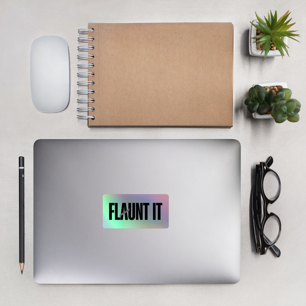 Flaunt It holographic vinyl sticker with 3D logo effect applied to a silver laptop on a desk with office supplies.