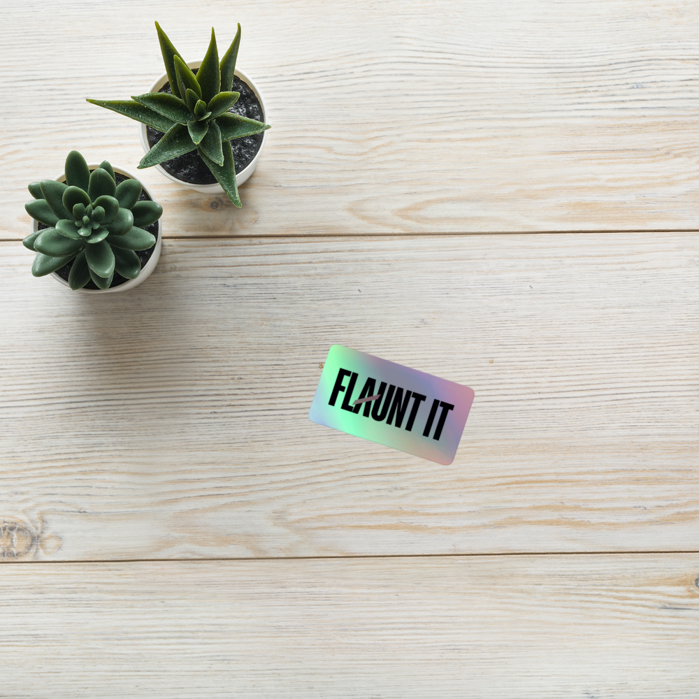 Flaunt It holographic vinyl sticker with black logo on a light wood surface next to two small potted succulents