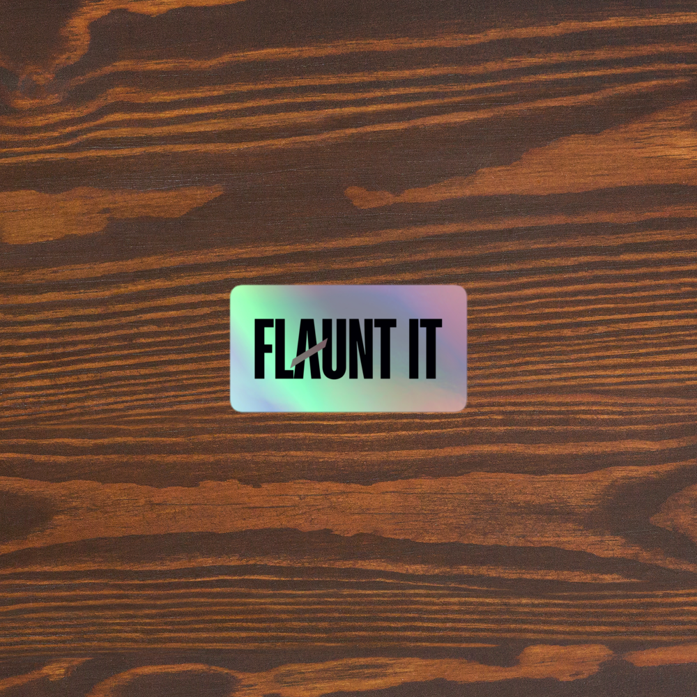 Flaunt It holographic vinyl logo sticker with a 3D embossed effect placed on a dark wood grain surface.