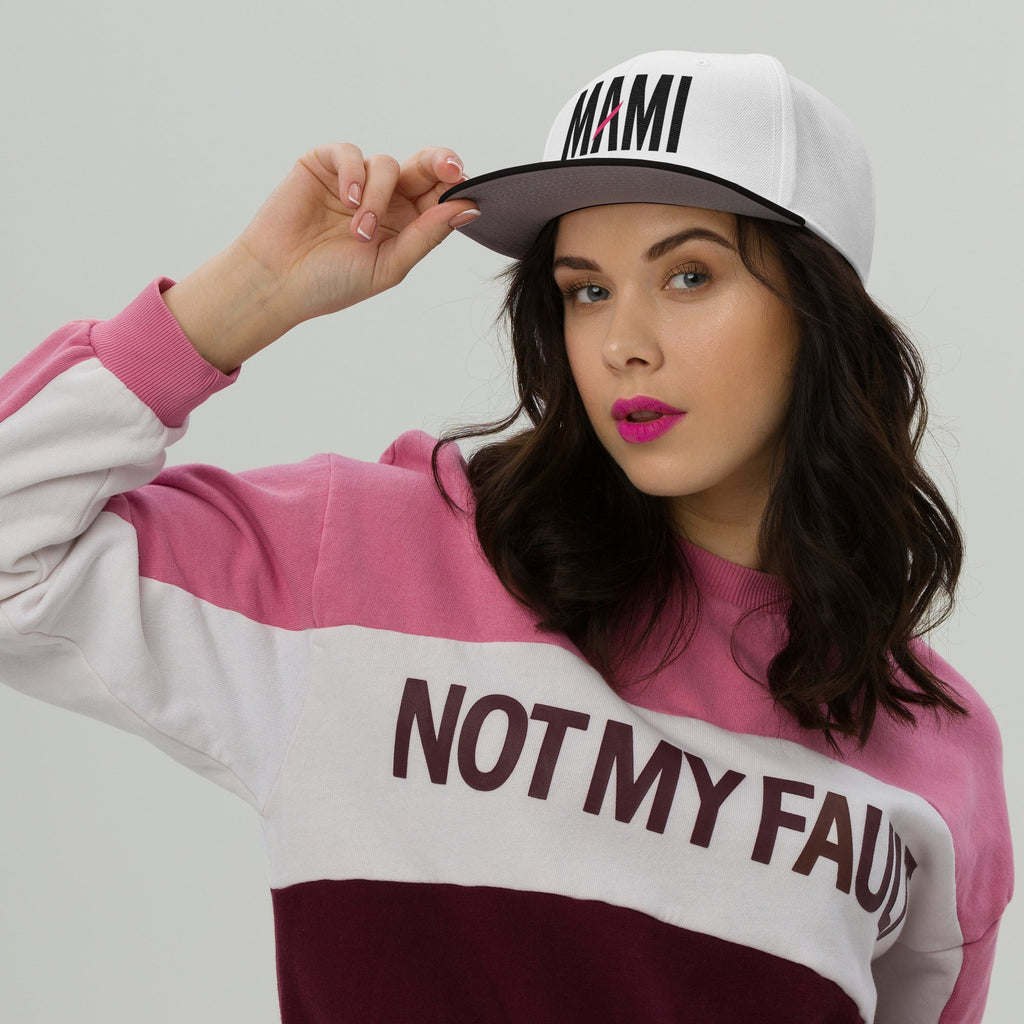 Flaunt It Mami embroidered white snapback hat with black text and pink slash detail worn by a woman in a pink sweater
