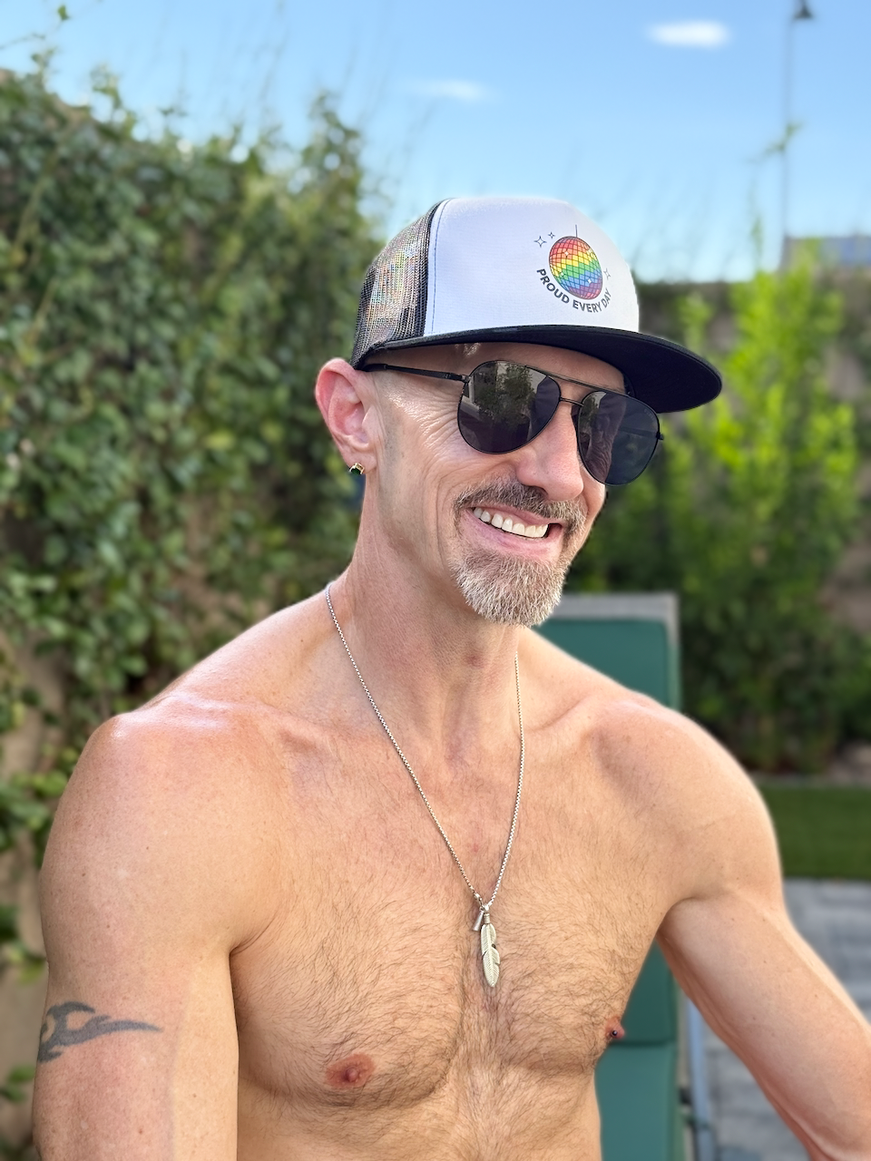 Flaunt It unisex structured trucker cap with a rainbow mirrorball graphic worn by a smiling man in sunglasses