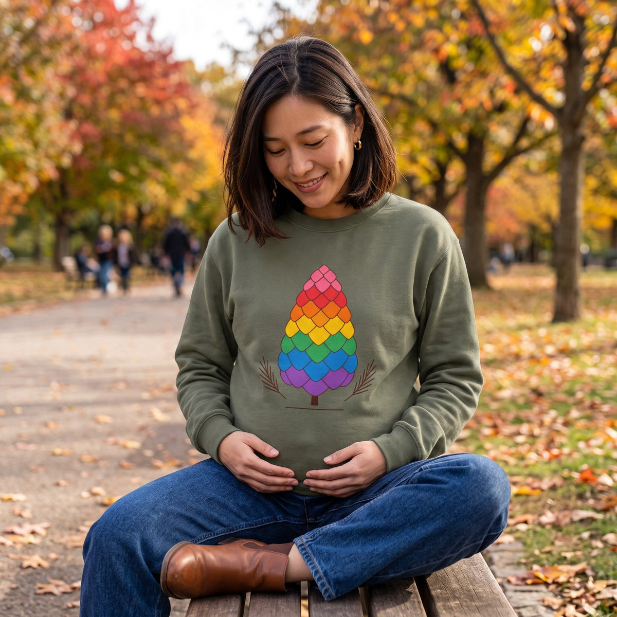 Flaunt It olive green heavyweight long sleeve shirt with a rainbow pinecone graphic, worn by a woman in a park.