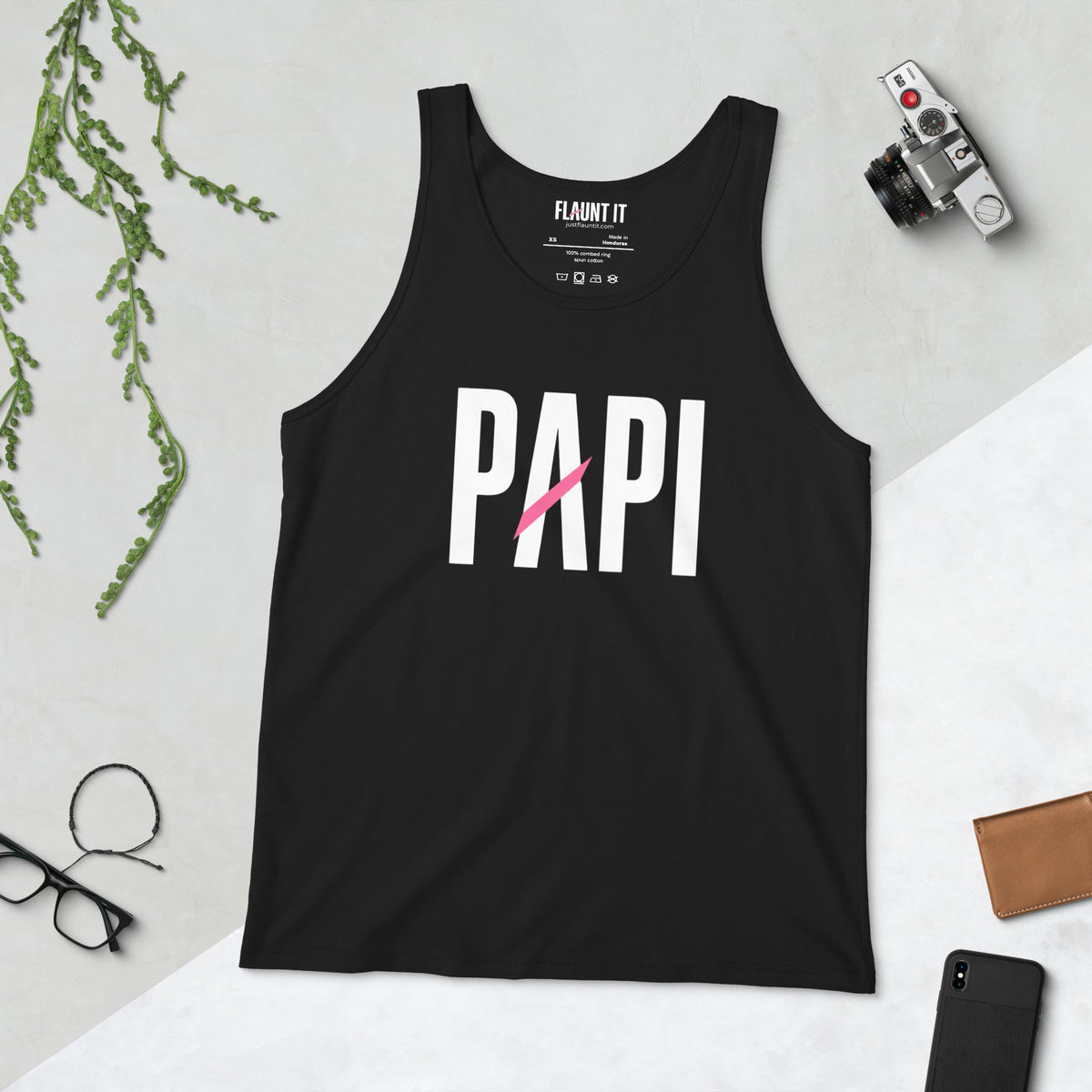 Flaunt It black unisex tank top with white PAPI text and a pink slash graphic on a flat lay background.