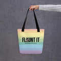 Flaunt It pastel rainbow zigzag tote bag with black handles and bold logo held by a hand against a grey background.