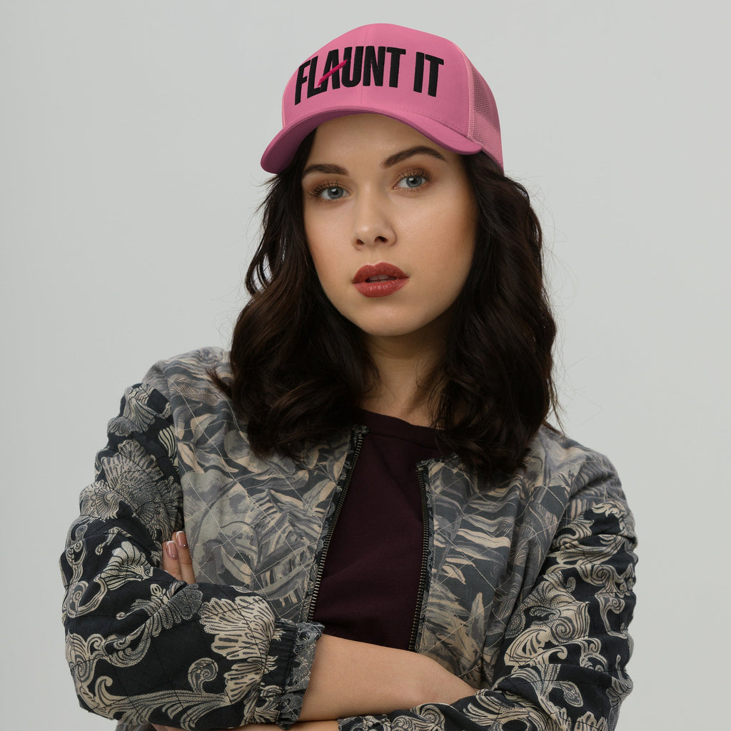 A woman wearing a pink Flaunt It embroidered logo hat with a mesh back and curved visor against a grey background.