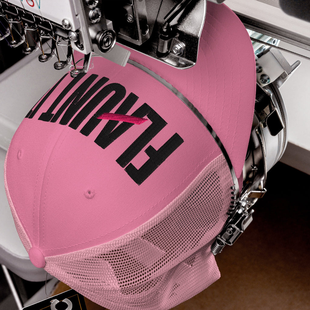 Flaunt It pink mesh back baseball cap with black embroidered logo being processed on an industrial embroidery machine