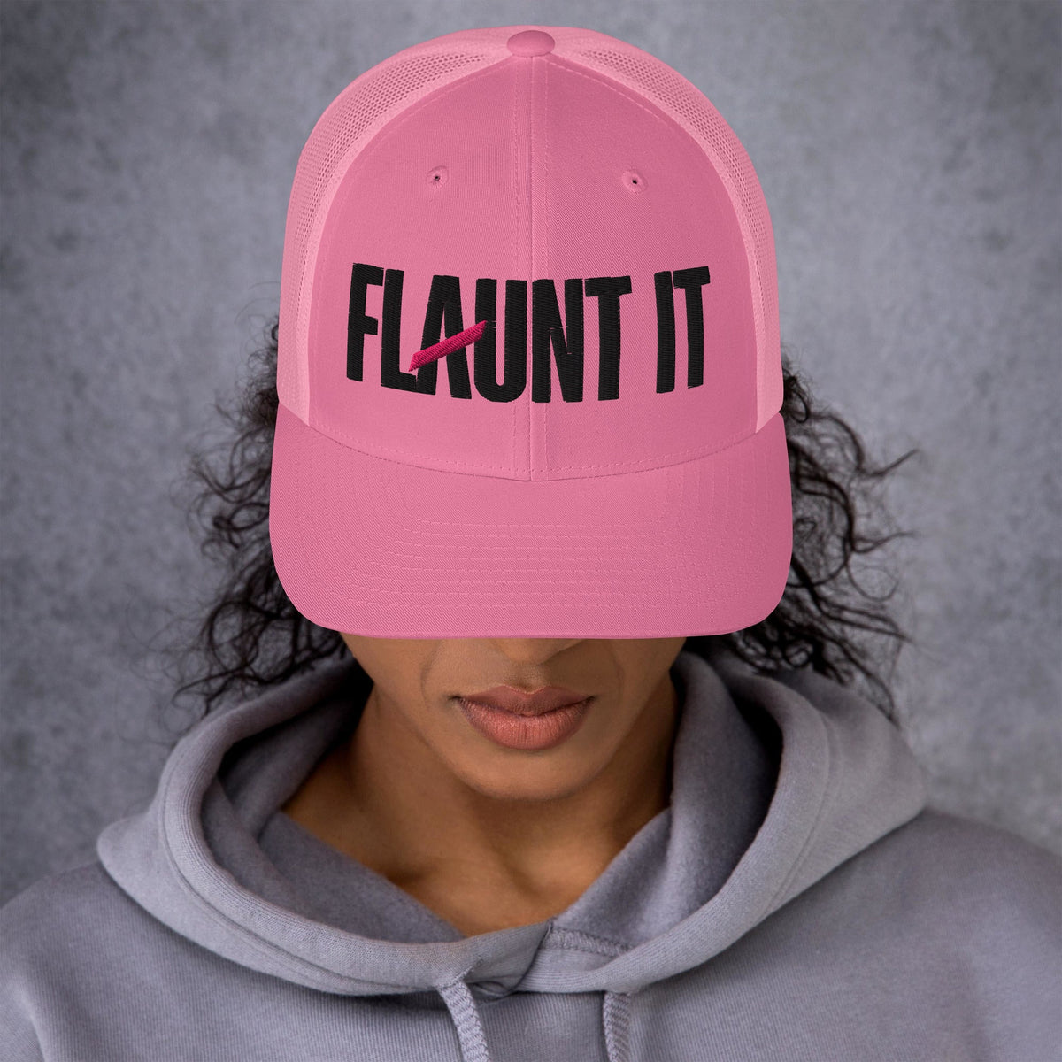 Flaunt It unisex pink mesh-back trucker hat with black embroidered wordmark logo worn by a person in a grey hoodie