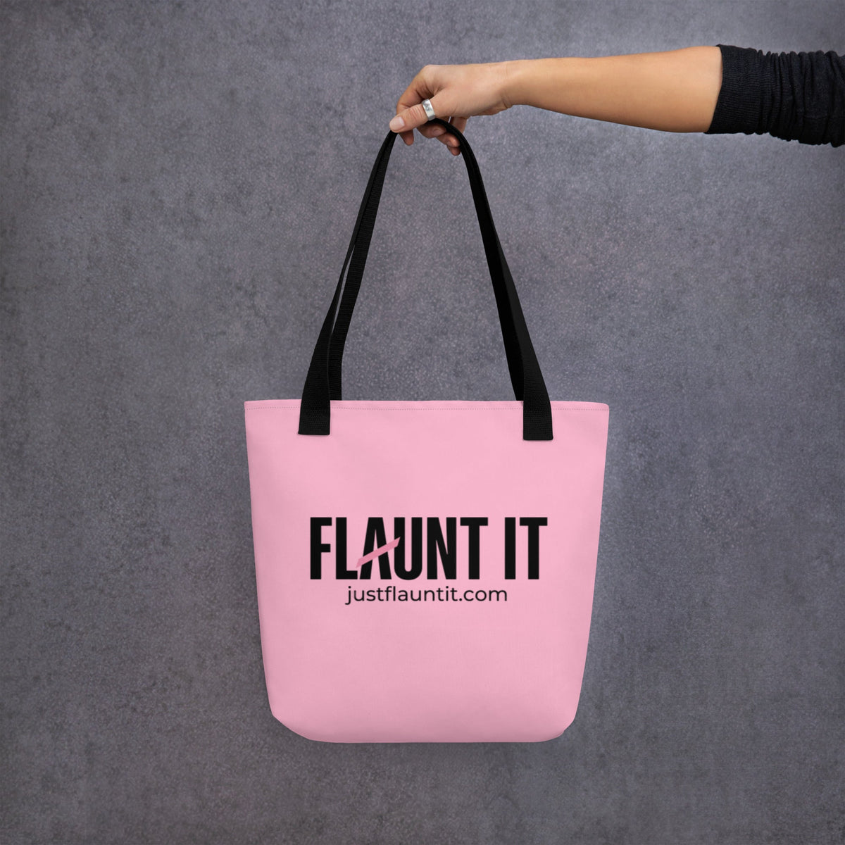 Flaunt It pink polyester canvas tote bag with black logo and durable black cotton handles held by a hand