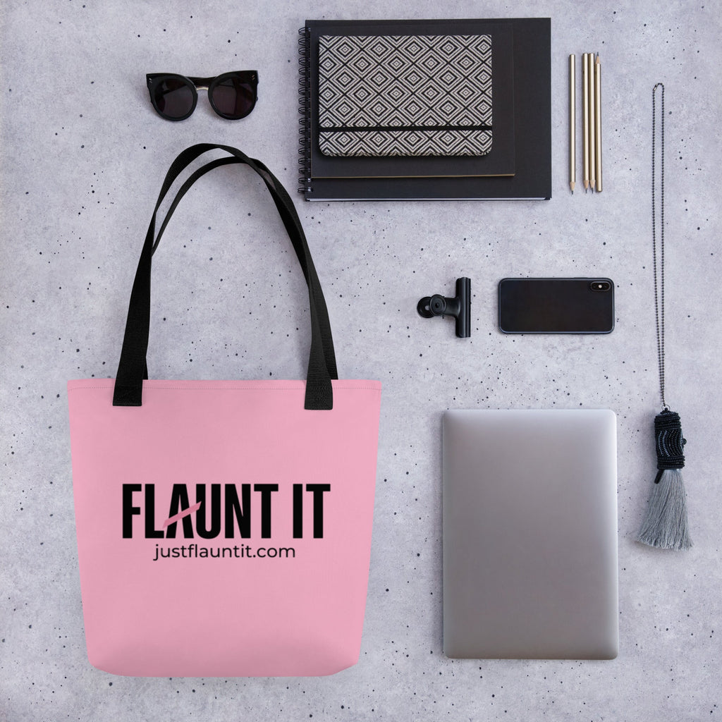 Flaunt It pink polyester canvas tote bag with black logo and handles, displayed on a grey desk with office supplies.