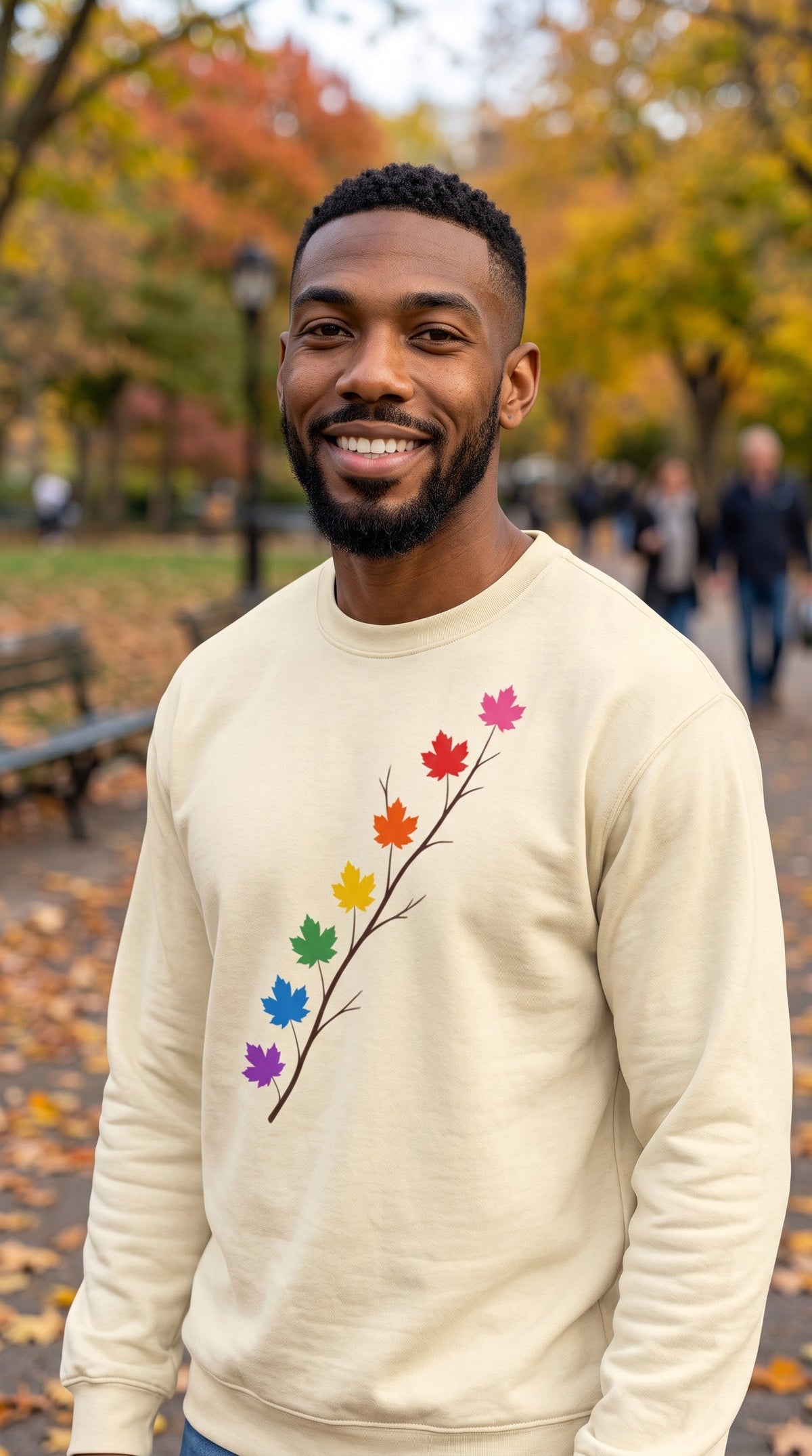 A man wearing a Flaunt It cream heavyweight long sleeve shirt with a pride maple leaf branch design in a park.