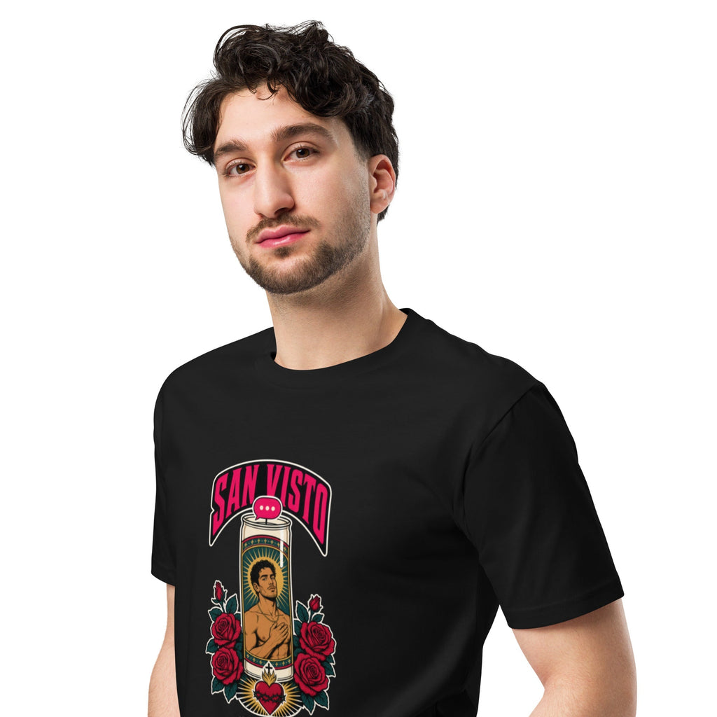 Three-quarter front view of a model wearing a black San Visto premium unisex T-shirt with a devotional prayer-candle illustration of a male saint, pink SAN VISTO headline, red roses and a sacred heart.