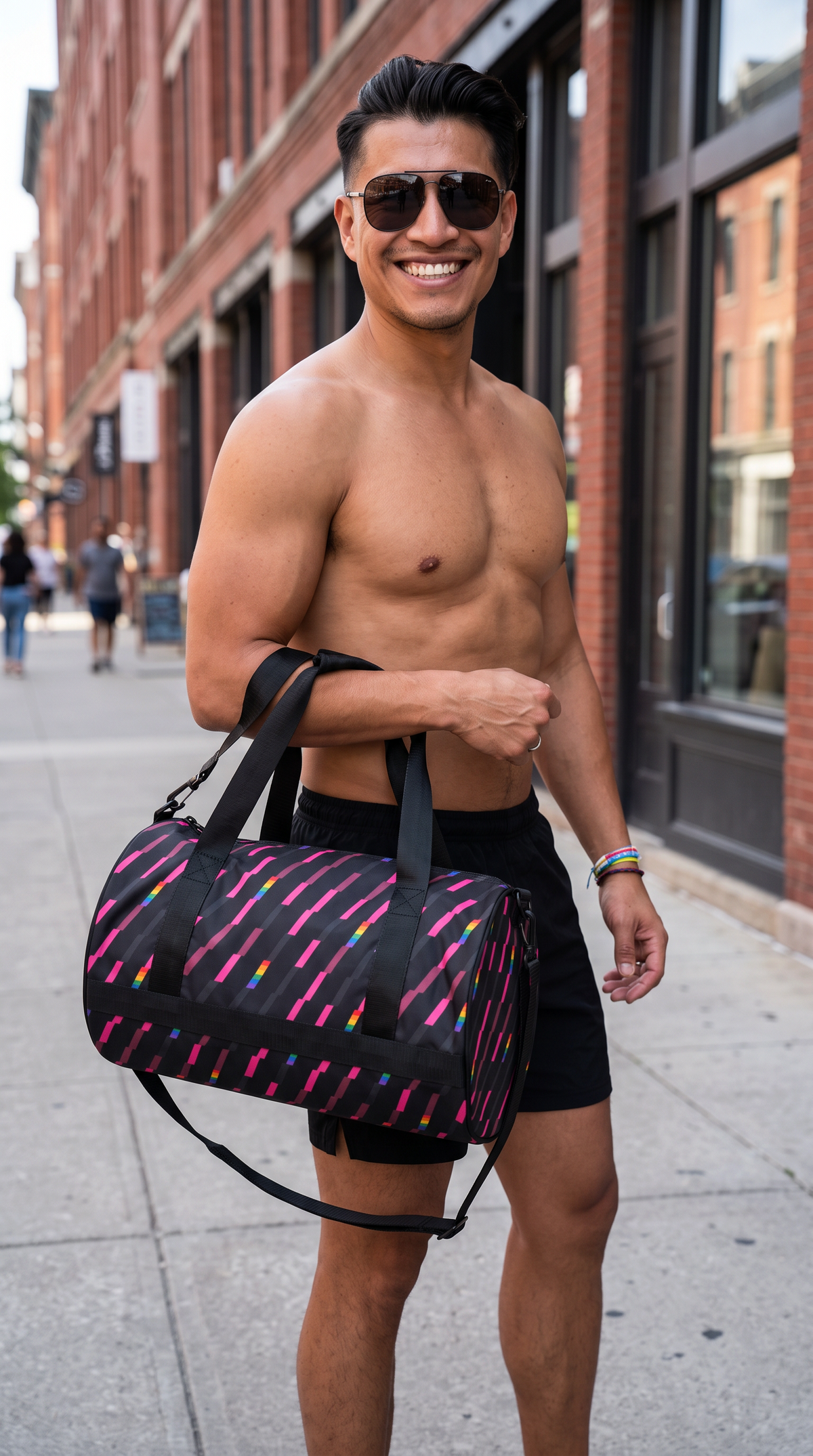 A smiling man carrying a Flaunt It Signature Monogram gym bag featuring a charcoal base with pink and rainbow stripes.