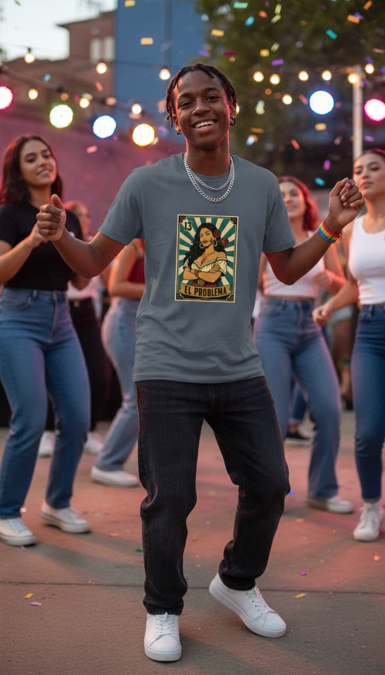 A smiling man in a petrol blue El Problema premium unisex T-shirt with a vintage loteria card design of a woman with roses, EL PROBLEMA text and number 13, dancing joyfully at a fun dance party with friends and colorful lights.
