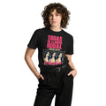 Front view of a model wearing a black Todas Se Llaman Igual premium unisex T-shirt with a lineup panel of three identical women with long dark hair and gold hoop earrings under a pink TODAS SE LLAMAN IGUAL headline.