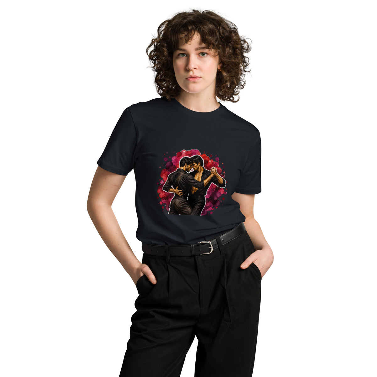 Front view of a smiling model wearing a navy Una Cancion Mas premium unisex T-shirt with a watercolor illustration of two women slow dancing against a magenta splash.