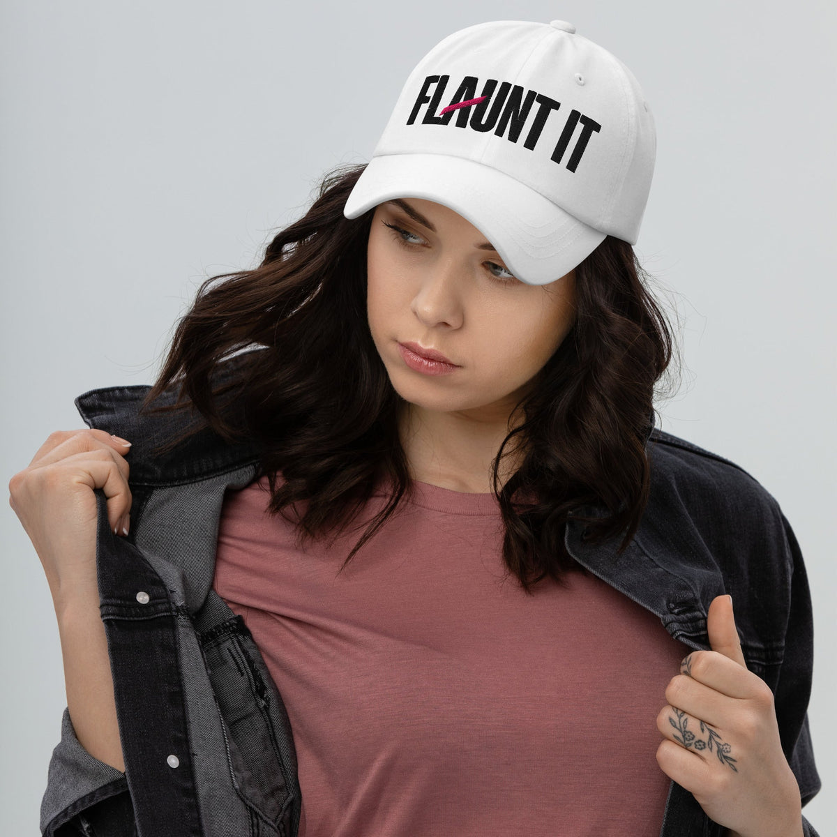 Woman wearing a white Flaunt It logo hat with a curved visor and embroidered wordmark, styled with a denim jacket.