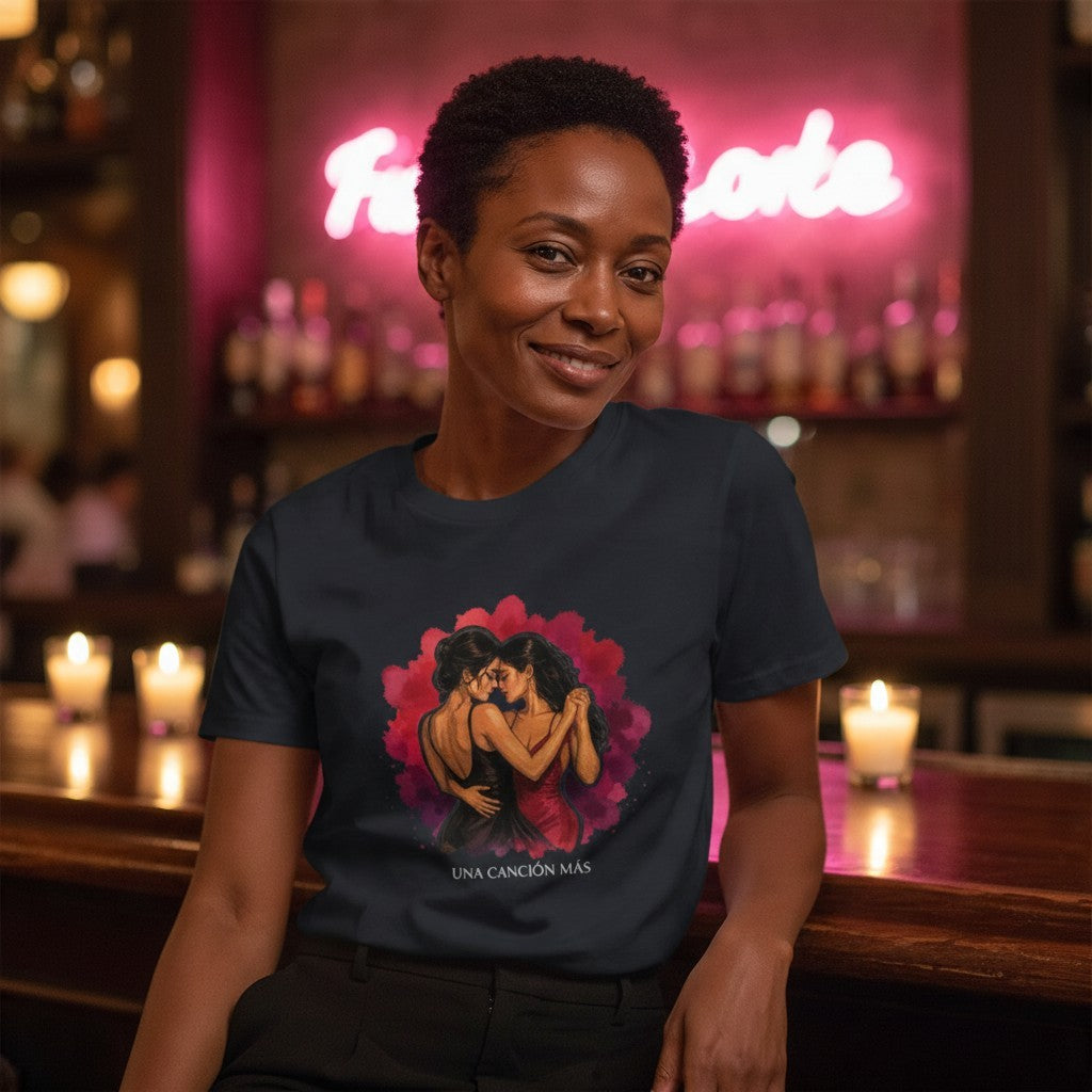 Smiling woman wearing the Una Canción Más Premium Unisex T-Shirt in Navy at a candle-lit bar, close up on the UNA CANCIÓN MÁS watercolor two women dancing design