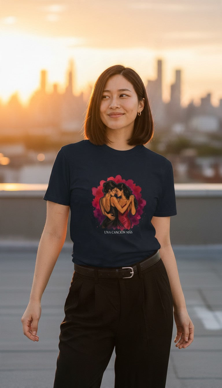 Woman wearing the Una Canción Más Premium Unisex T-Shirt in Navy on a rooftop at golden hour, with the UNA CANCIÓN MÁS watercolor two women dancing design